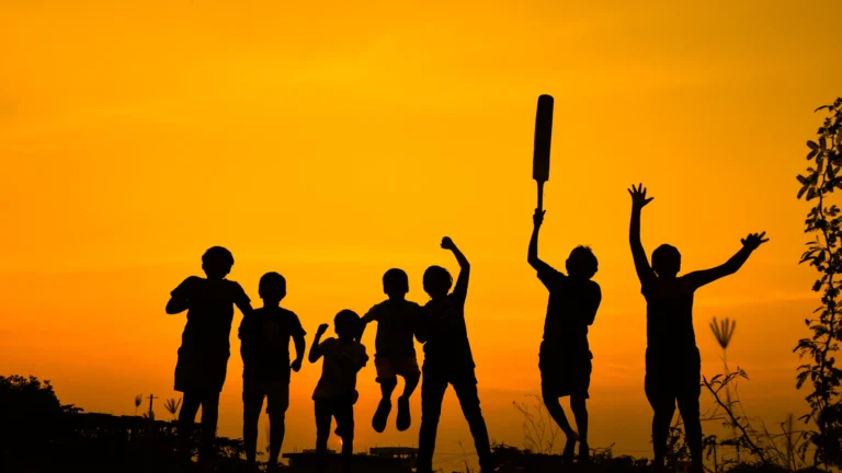 Children celebrating with a cricket bat at sunset